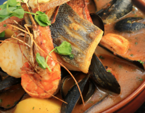 A bowl of Bouillabaisse, featuring fresh seafood, vegetables, and aromatic herbs.