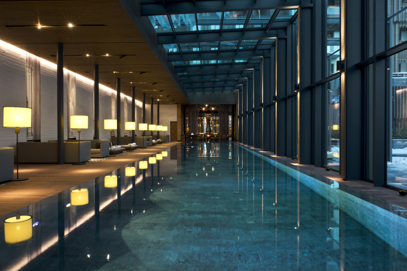 Indoor swimming pool at The Chedi Andermatt, with serene lighting, elegant design, and views of the snow-covered Swiss Alps through large windows.