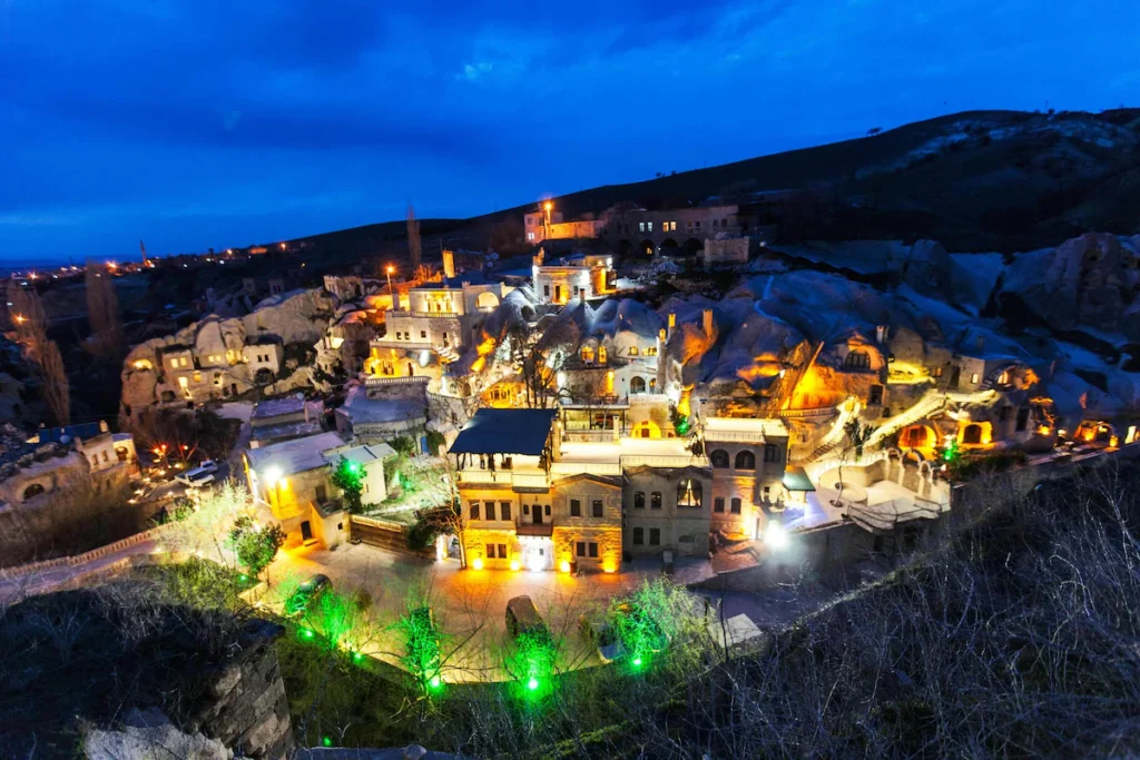 Gamirasu Cave Hotel Turkey - Exterior view at dusk with warm evening lighting illuminating ancient cave dwellings in Cappadocia