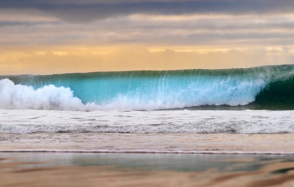 Surfer catching a wave at Carcavelos Beach with the historic Fort of São Julião da Barra in the background.