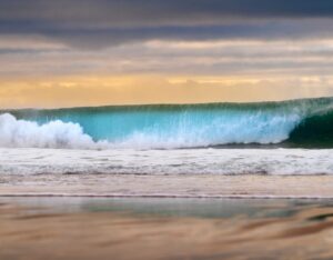 Surfer catching a wave at Carcavelos Beach with the historic Fort of São Julião da Barra in the background.