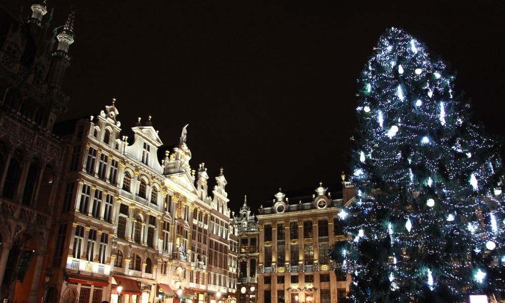 n assortment of Belgian Christmas pastries and chocolates displayed at a stall in the Brussels Christmas market, with festive lights and decorations in the background.