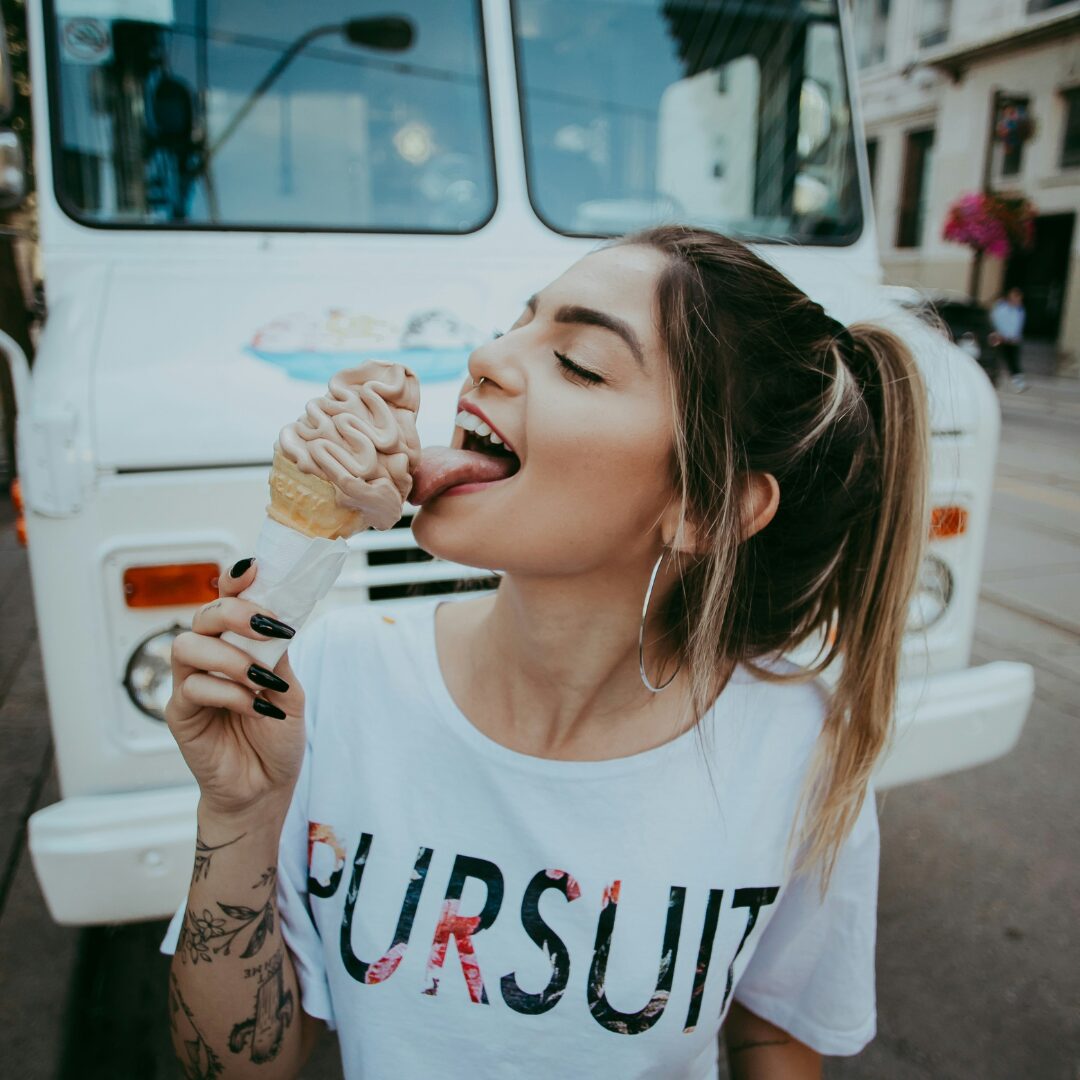 A young woman licking an ice cream in front of an old bus