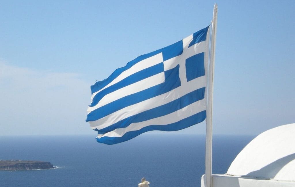 Greek flag waving with the azure sea in the background, symbolizing Greece's rich cultural and maritime heritage