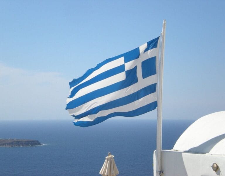 Greek flag waving with the azure sea in the background, symbolizing Greece's rich cultural and maritime heritage