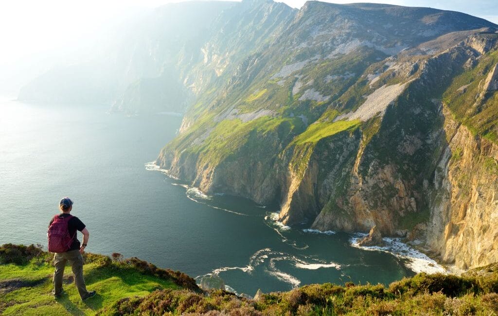 Person standing at the iconic Irish cliffs overlooking the sea, symbolizing the exploration of Ireland's natural and cultural beauty