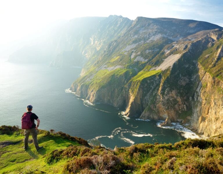 Person standing at the iconic Irish cliffs overlooking the sea, symbolizing the exploration of Ireland's natural and cultural beauty