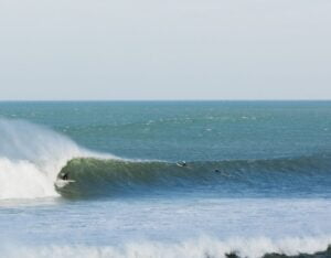 Surfer riding the famous left-hand wave in Mundaka, with the Basque Country's stunning scenery in the background.