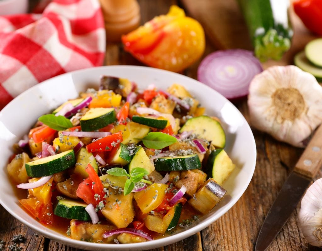 A beautifully arranged plate of traditional Ratatouille with thinly sliced vegetables, including zucchini, eggplant, and bell peppers, baked to perfection with a golden finish.