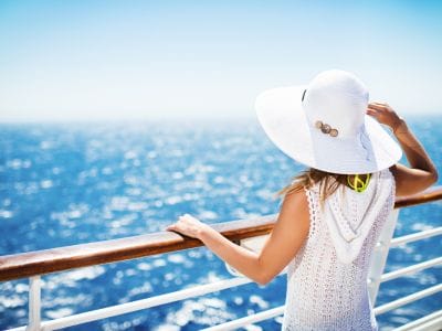 Woman standing at cruise ship railing gazing into the ocean horizon