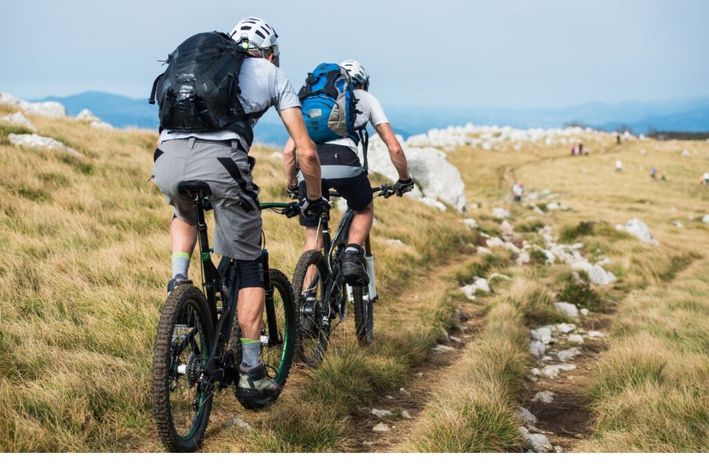 Two cyclists with backpacks riding through mountainous terrain in Germany.