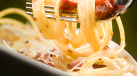 A close-up of authentic Spaghetti Carbonara with creamy sauce, crispy guanciale, and a dusting of Pecorino Romano, garnished with freshly ground black pepper.