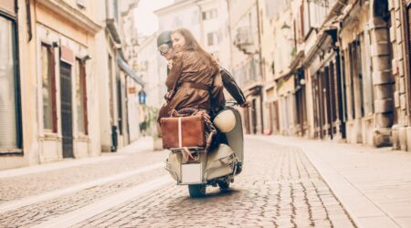 A couple riding a classic Italian moped through a narrow, picturesque alleyway in Italy, surrounded by historic buildings.