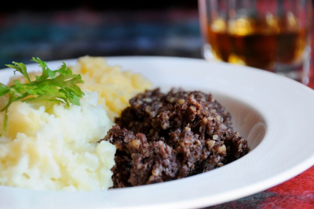 A traditional Scottish Haggis, sliced open, revealing a rich filling of lamb offal, oats, and spices, served with mashed potatoes and turnips