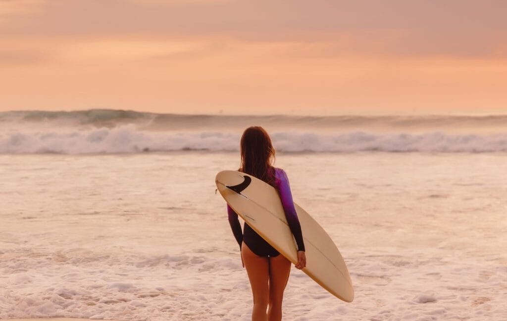 A surfer catching a wave at sunrise in Lagos, Portugal, with the stunning Algarve coastline in the background.